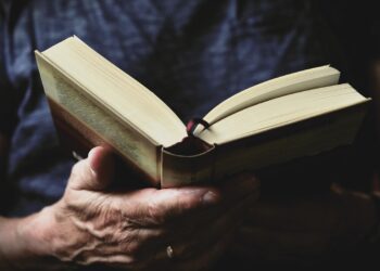 Eski bir kitabı elleriyle açıp okuyan bir kişinin yakın plan görüntüsü.