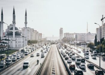 Şehir içi yoğun trafikte seyreden otomobiller ve solda büyük bir cami.