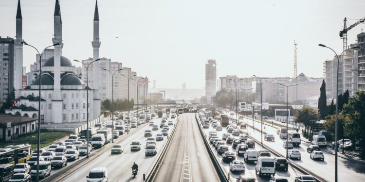 Şehir içi yoğun trafikte seyreden otomobiller ve solda büyük bir cami.