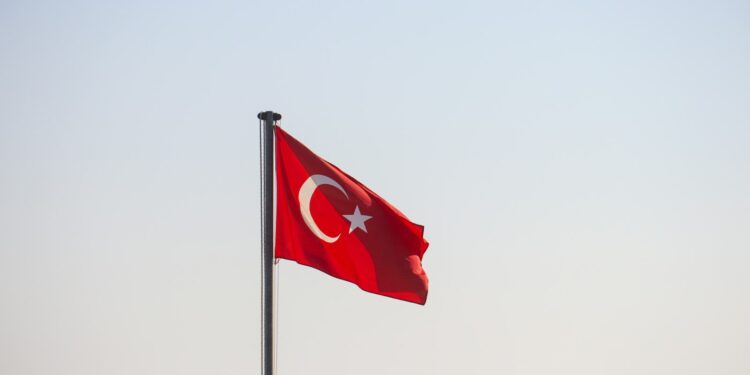 Açık mavi gökyüzü önünde dalgalanan kırmızı renkli Türk bayrağı.