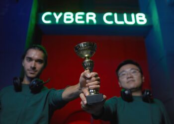 Cyber Club tabelası altında ellerinde kupa tutan iki genç oyuncu.