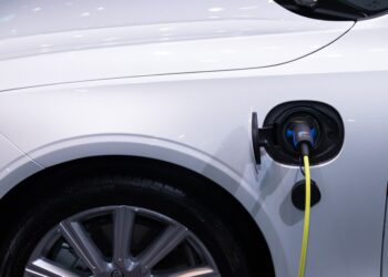 Şarj kablosu takılı olan beyaz renkli elektrikli bir otomobilin yandan görünümü.