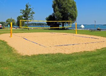 Masmavi gökyüzü altında kum zemin üzerine kurulu voleybol sahası ve filesi.