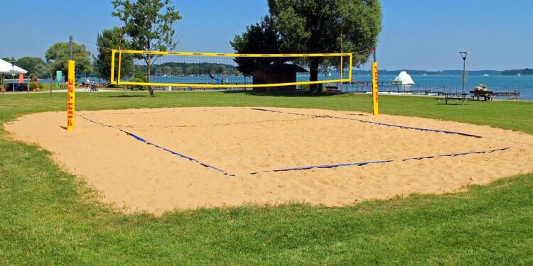 Masmavi gökyüzü altında kum zemin üzerine kurulu voleybol sahası ve filesi.