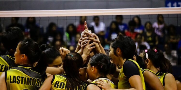 Sarı siyah formalı kadın voleybol takımı oyuncuları ellerini üst üste koymuş kutlama yapıyor.