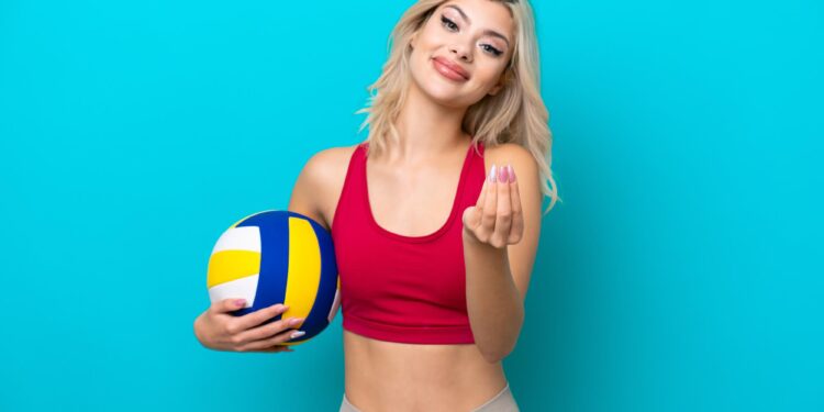 Mavi arka plan önünde elinde voleybol topu tutan sarışın sporcu.