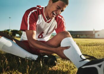Saha kenarında oturup sakatlanan bacağını tutarak acı içinde bağıran futbolcu.