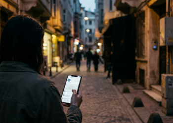 Akşam karanlığında sokakta yürürken telefonundaki sosyal medya paylaşımını inceleyen genç bir kadın.