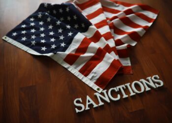 Ahşap masa üzerinde duran ABD bayrağı ve sanctions yazısı.
