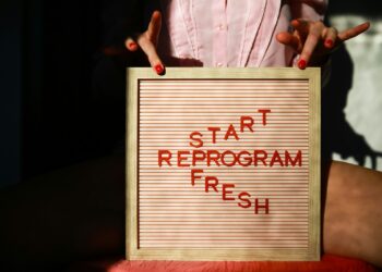 Pembe fon önünde 'Start Reprogram Fresh' yazılı panoyu tutan kadın elleri.