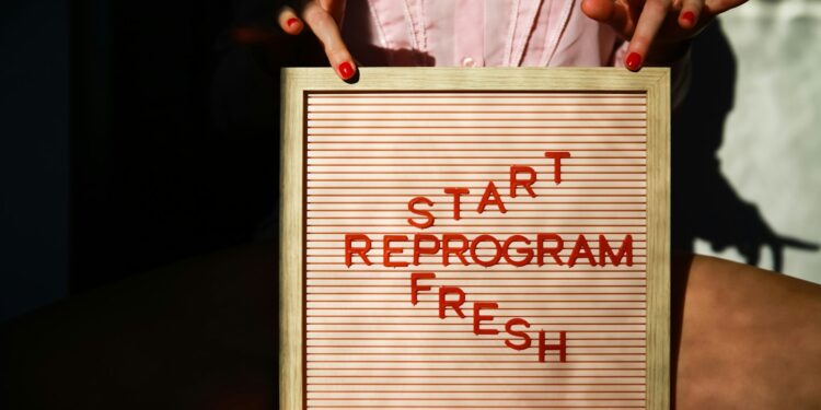 Pembe fon önünde 'Start Reprogram Fresh' yazılı panoyu tutan kadın elleri.