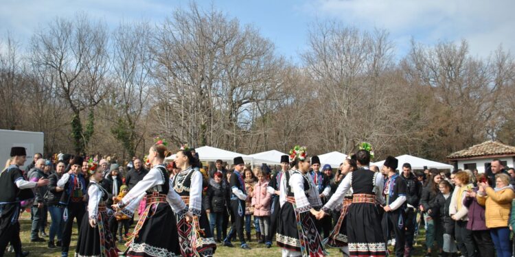 Geleneksel kıyafetler giymiş halk dansı ekibi açık havada el ele tutuşarak dans ediyor.