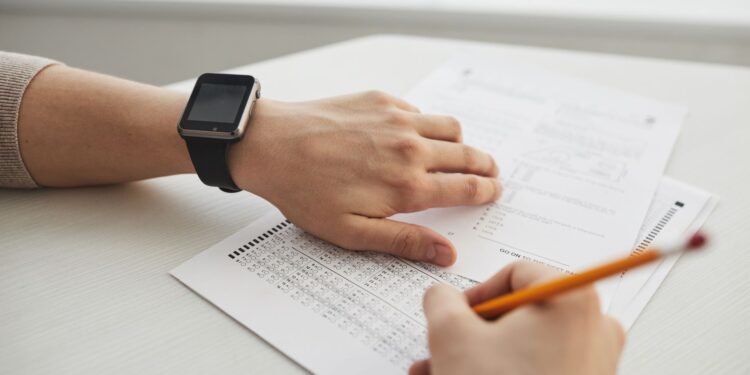 Akıllı saat takan bir aday test kağıdına optik form dolduruyor.