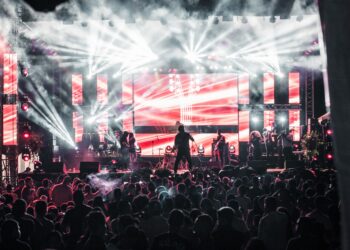 Afişli büyük bir sahnede canlı müzik performansı sergileyen müzik grubu ve kalabalık.