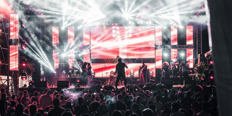 Afişli büyük bir sahnede canlı müzik performansı sergileyen müzik grubu ve kalabalık.