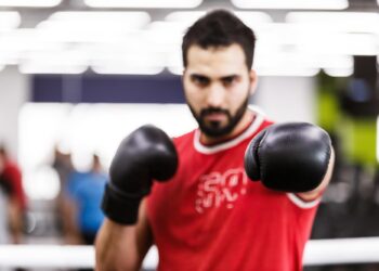 Kırmızı atlet giymiş, siyah boks eldivenleriyle kamera yönüne doğru yumruk atan erkek boksör.