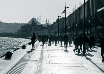 İstanbul sahilinde yürüyüş yapan insanlar ve uzaktaki silüet.