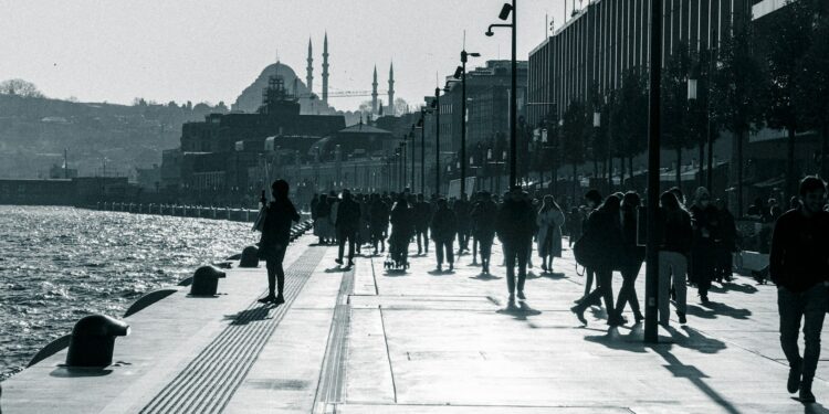 İstanbul sahilinde yürüyüş yapan insanlar ve uzaktaki silüet.
