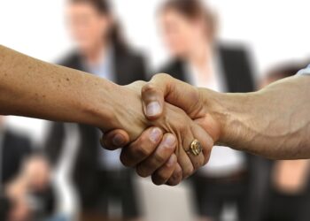 Bir grup insanin arka plandaki bulanik silueti esliginde tokalasan iki kisinin elleri