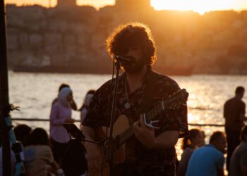 Gün batımında açık havada gitar çalan ve şarkı söyleyen bir müzisyen.