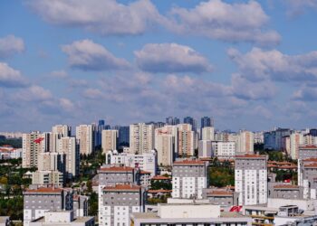 Bulutlu mavi gökyüzü altında çok katlı binalar ve modern şehir yerleşimi.