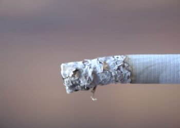 Gri arka plan önünde duran sigara izmariti ve külleri.