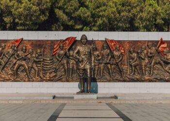 Bronz kabartma heykel duvarının önünde duran askeri komutan heykeli ve askerler.