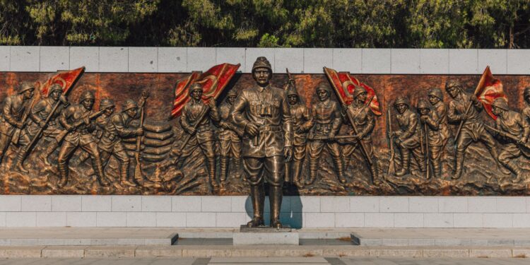 Bronz kabartma heykel duvarının önünde duran askeri komutan heykeli ve askerler.