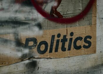 Yıpranmış bir ahşap duvar üzerinde 'Politics' yazısı ve kırmızı bir daire.