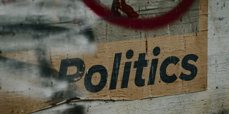 Yıpranmış bir ahşap duvar üzerinde 'Politics' yazısı ve kırmızı bir daire.