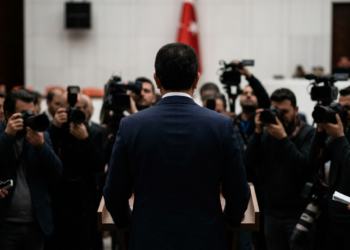Meclis kürsüsünde açıklama yapan siyasetçiyi takip eden basın mensupları arkadan görülüyor.